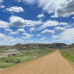 Dirt road, green landscape, and big blue skies with white clouds. Ft Peck, Montana.